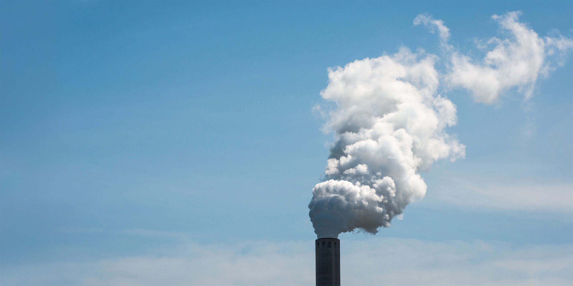 White smoke billowing from an industrial smokestack against a blue sky.