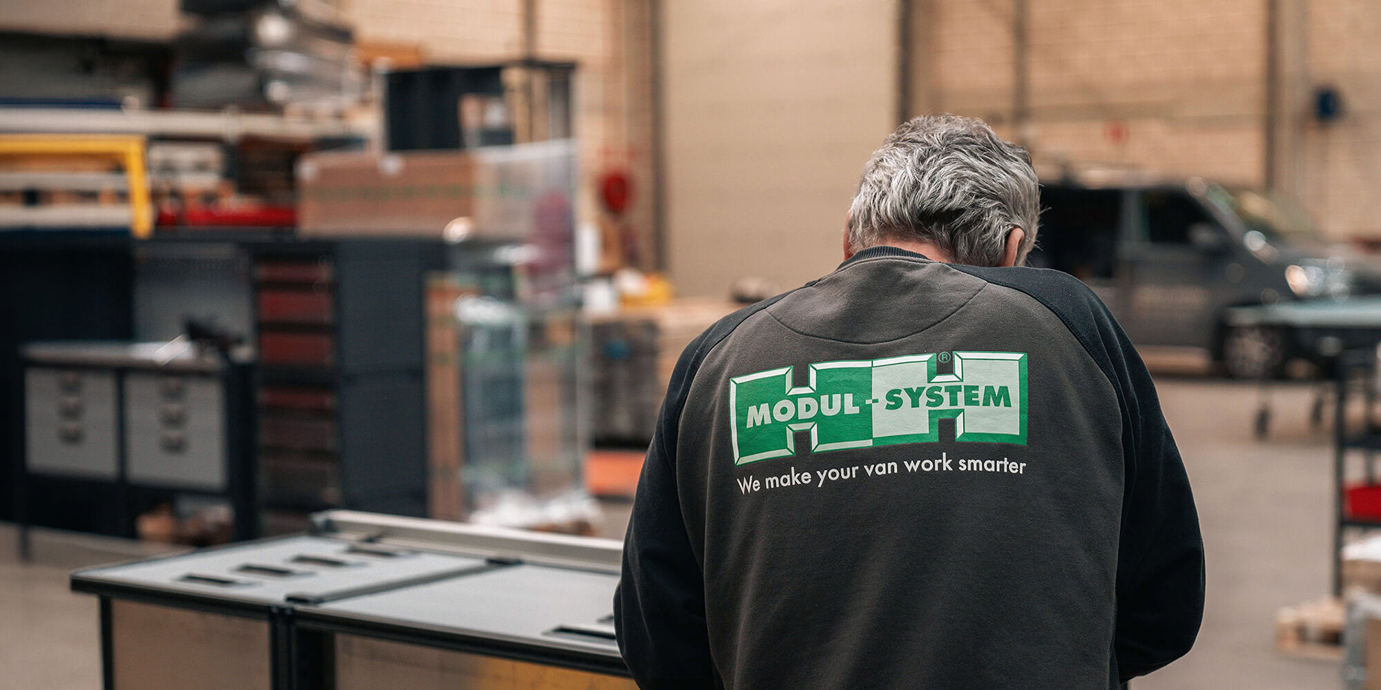 Modul-System employee wearing a Modul-System jacket in a bright industrial workshop.