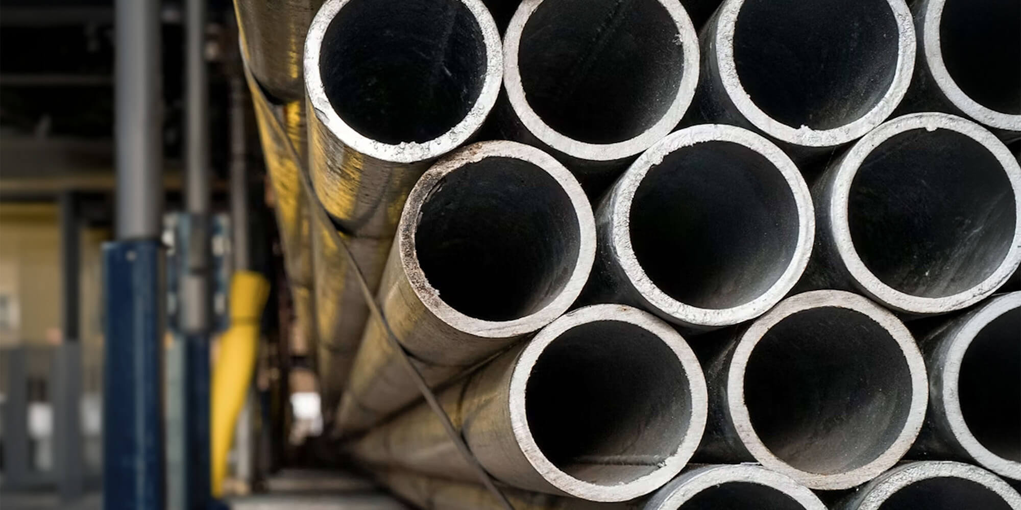A stack of hollow steel pipes neatly arranged in an industrial warehouse.
