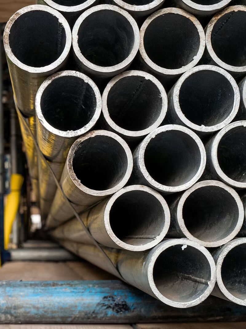 A stack of hollow steel pipes neatly arranged in an industrial warehouse.