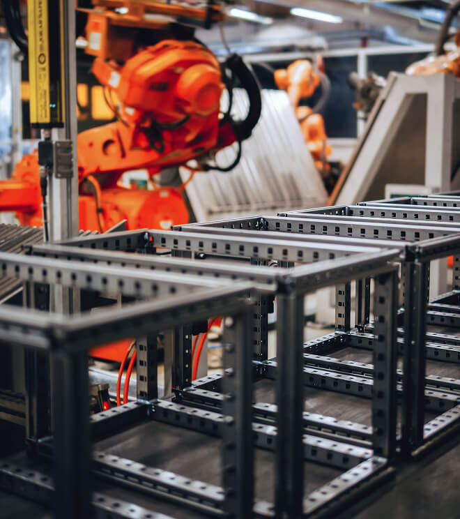 An orange robotic arm assembling metal frames on a factory production line.